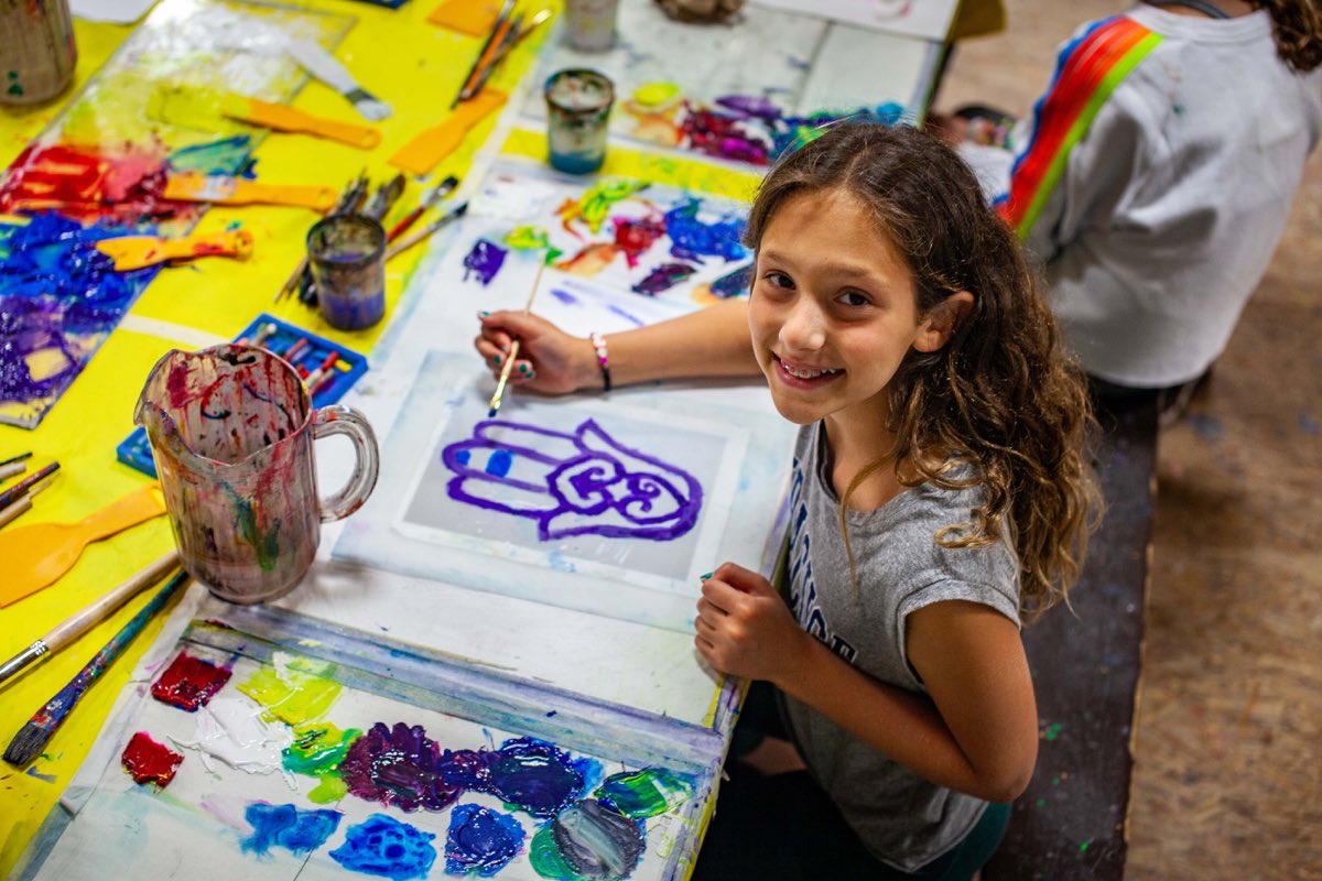 A camper painting a design at the arts and crafts table