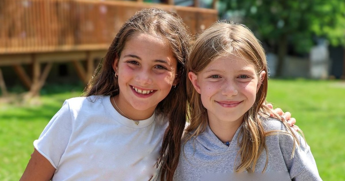 Two smiling girls with their arms around each other on the camp lawn