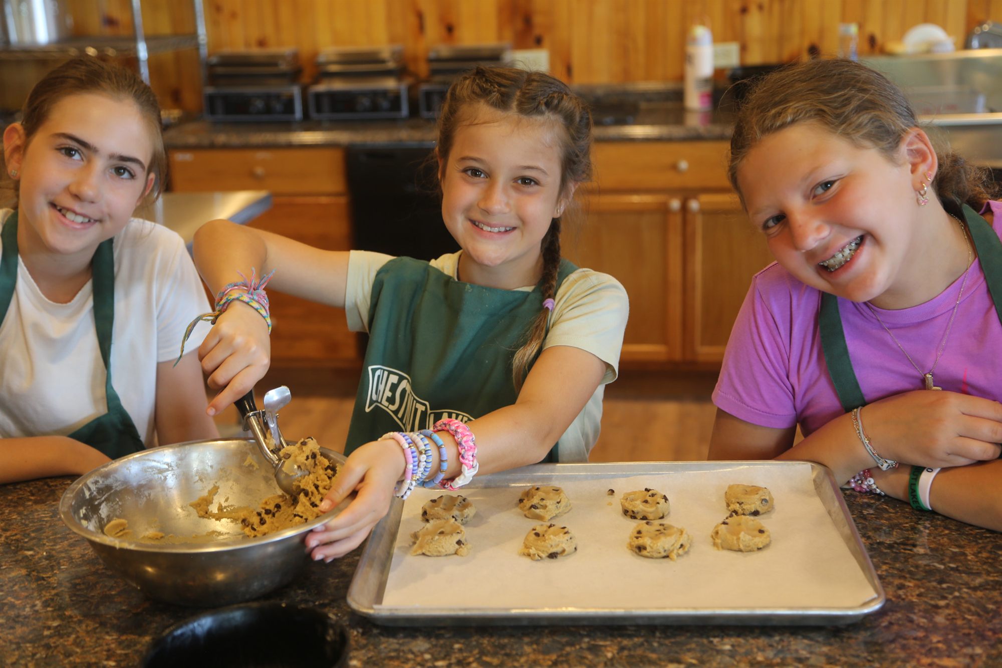 Campers baking cookies together at a long kitchen table