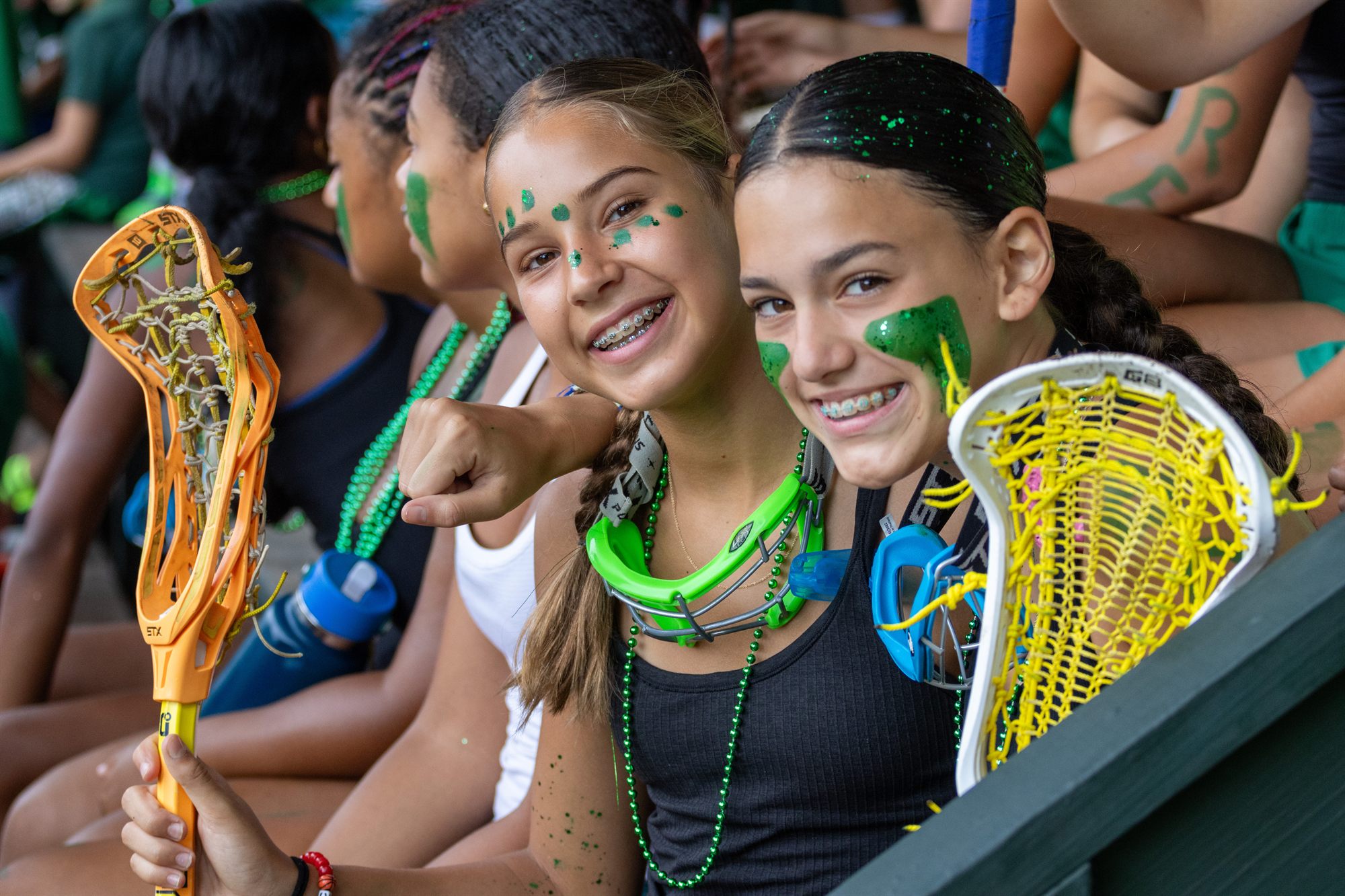 Two campers in green face paint grinning with their lacrosse sticks