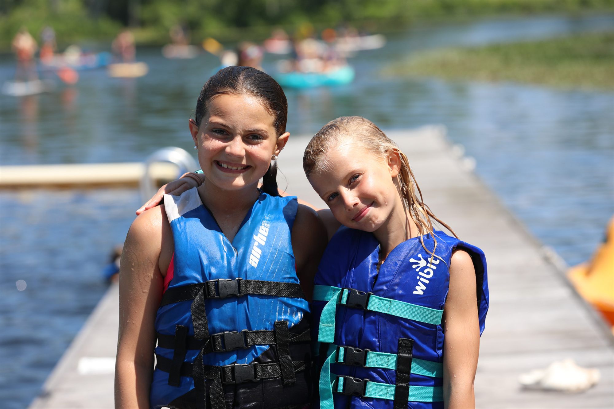 Two girls in life jackets smiling on the dock