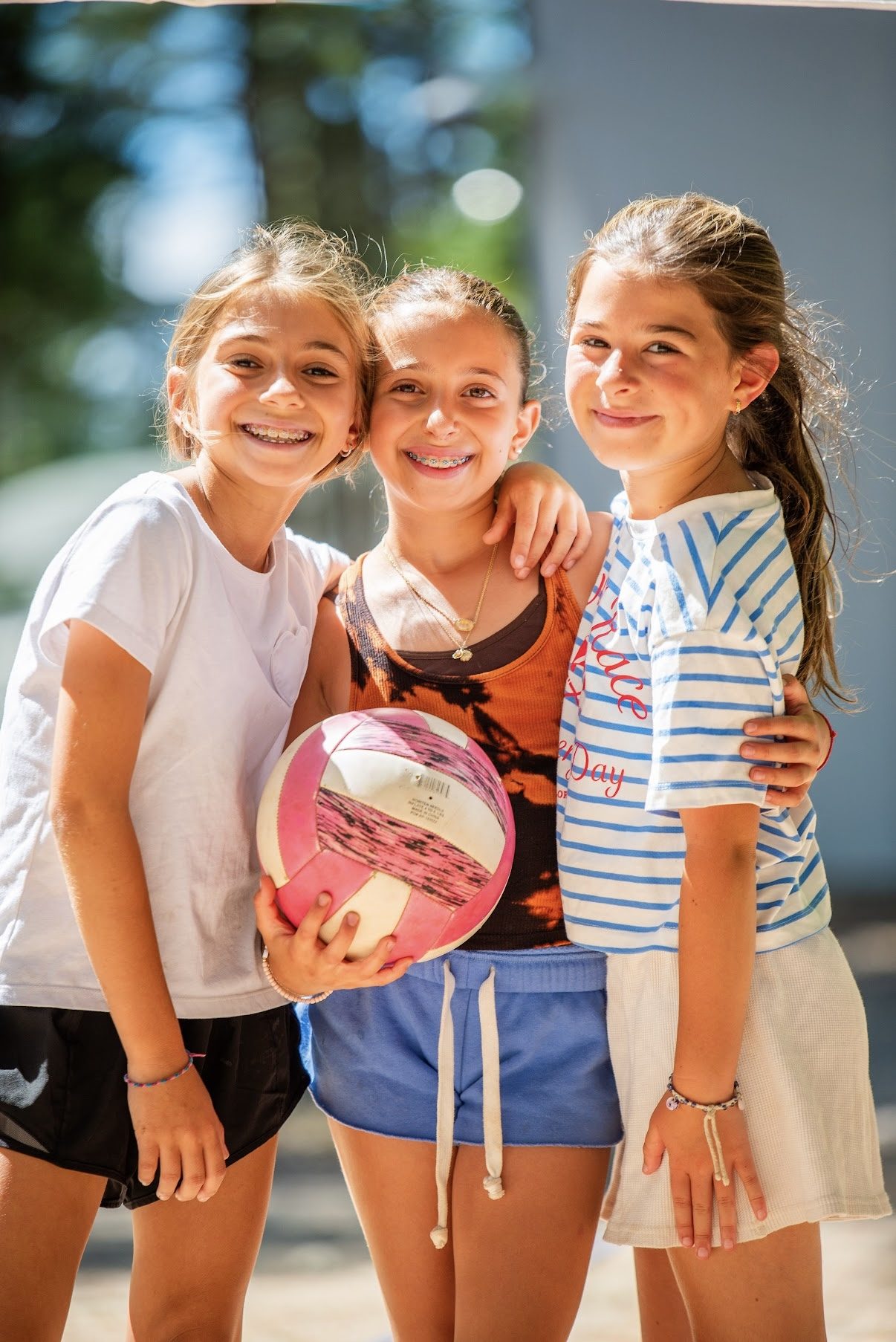 Three campers with their arms around each other holding a volleyball
