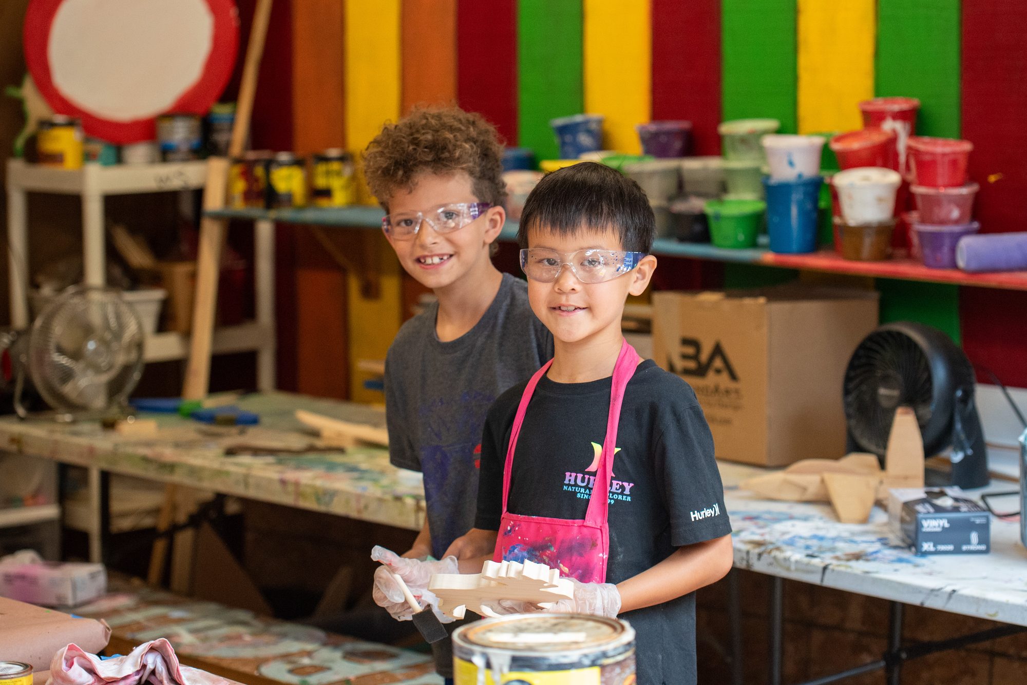 Two campers in aprons and goggles painting in the art shack
