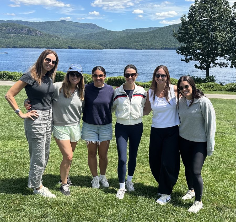 The Camp Specialists team together on the lawn above a mountain lake