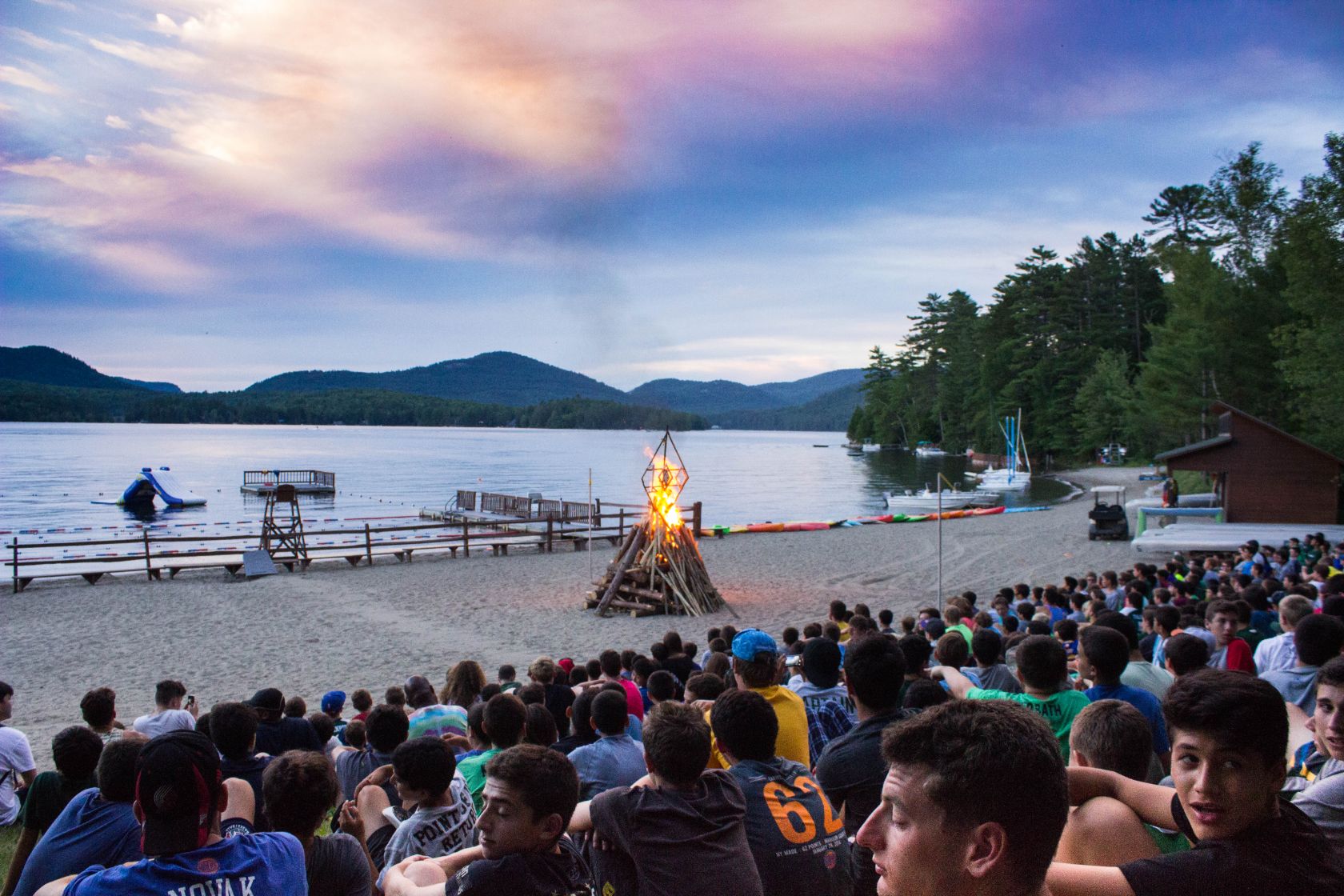 Campers gathered around a lakeside bonfire at dusk