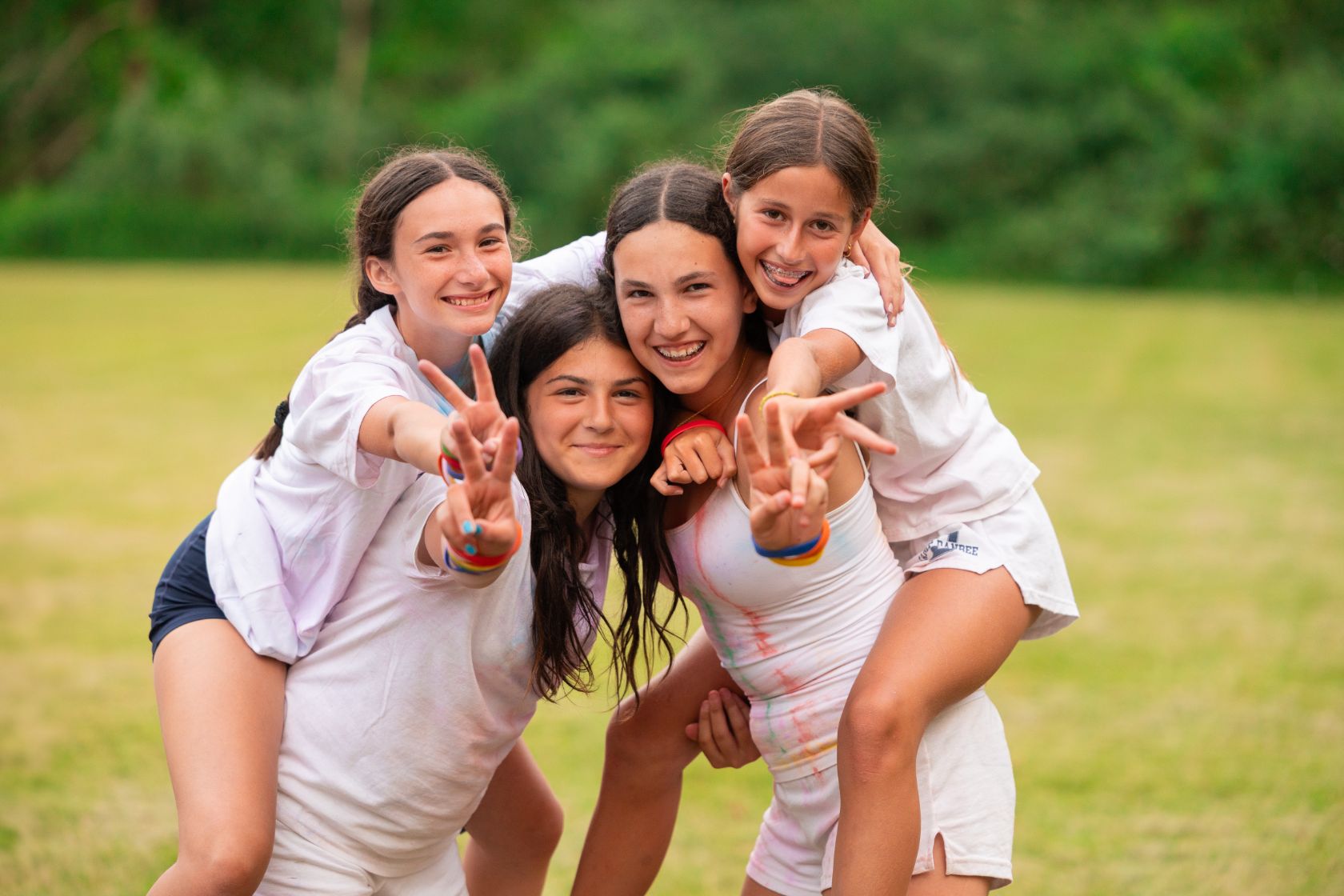 Four smiling campers arm in arm in a sunny field, flashing peace signs