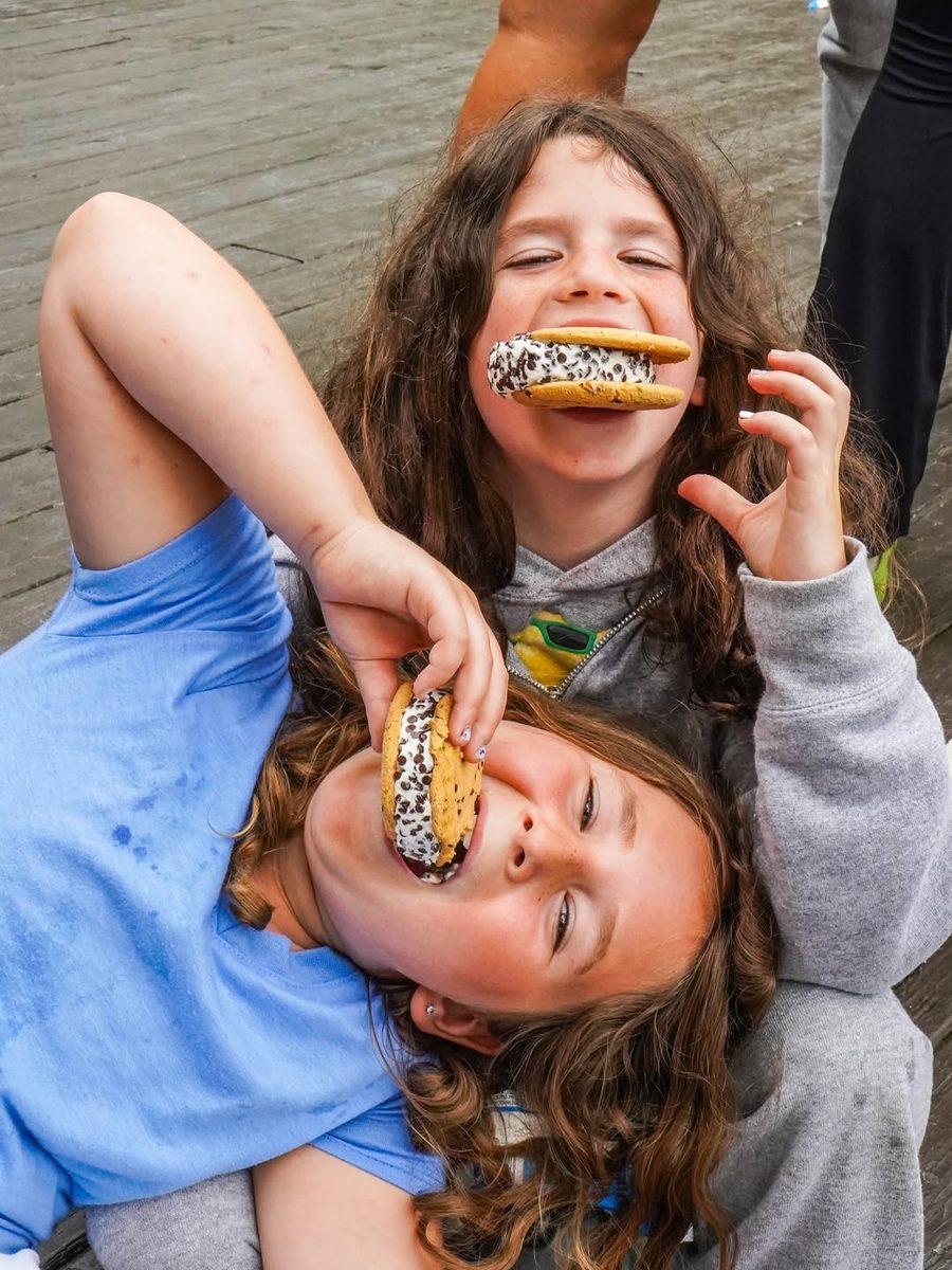 Two girls lying head to head on the ground, grinning with ice-cream sandwiches