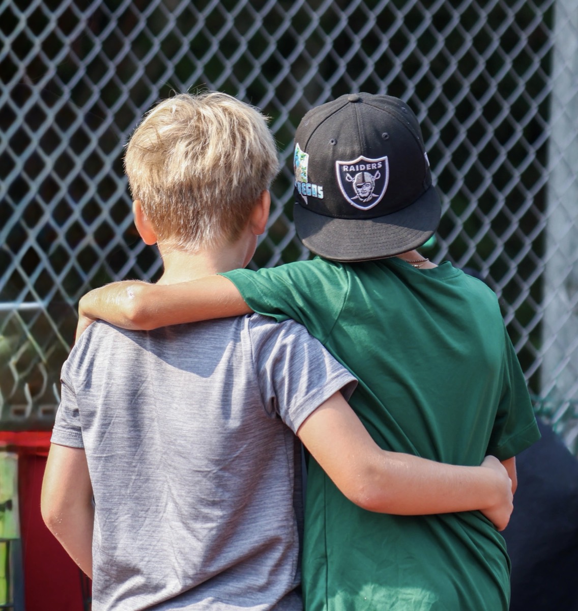 Two campers standing arm in arm, watching a game through a backstop fence