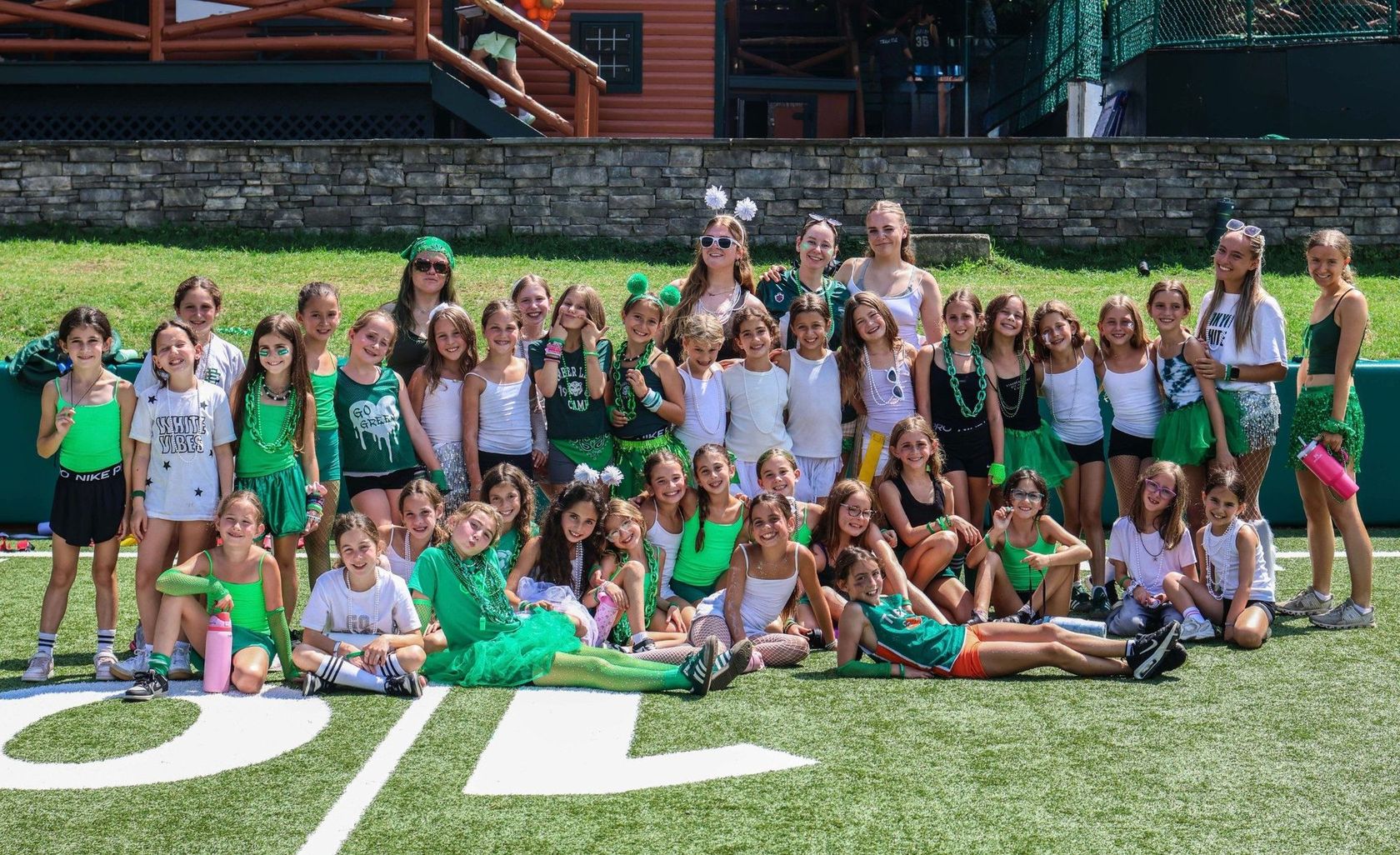 A big group of girls in green team colours posing together on the field for Color War