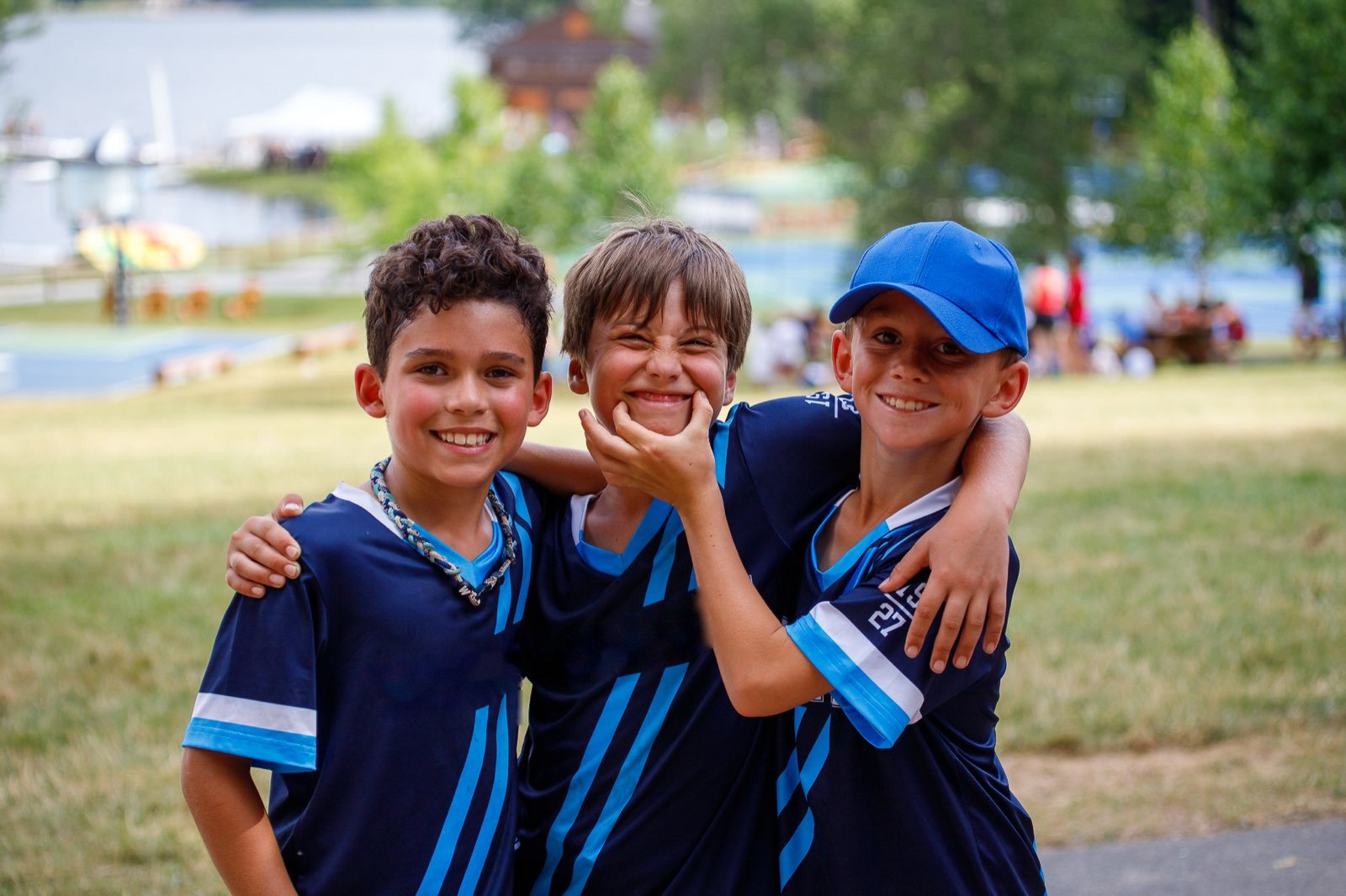 Three young campers in matching jerseys grinning arm in arm