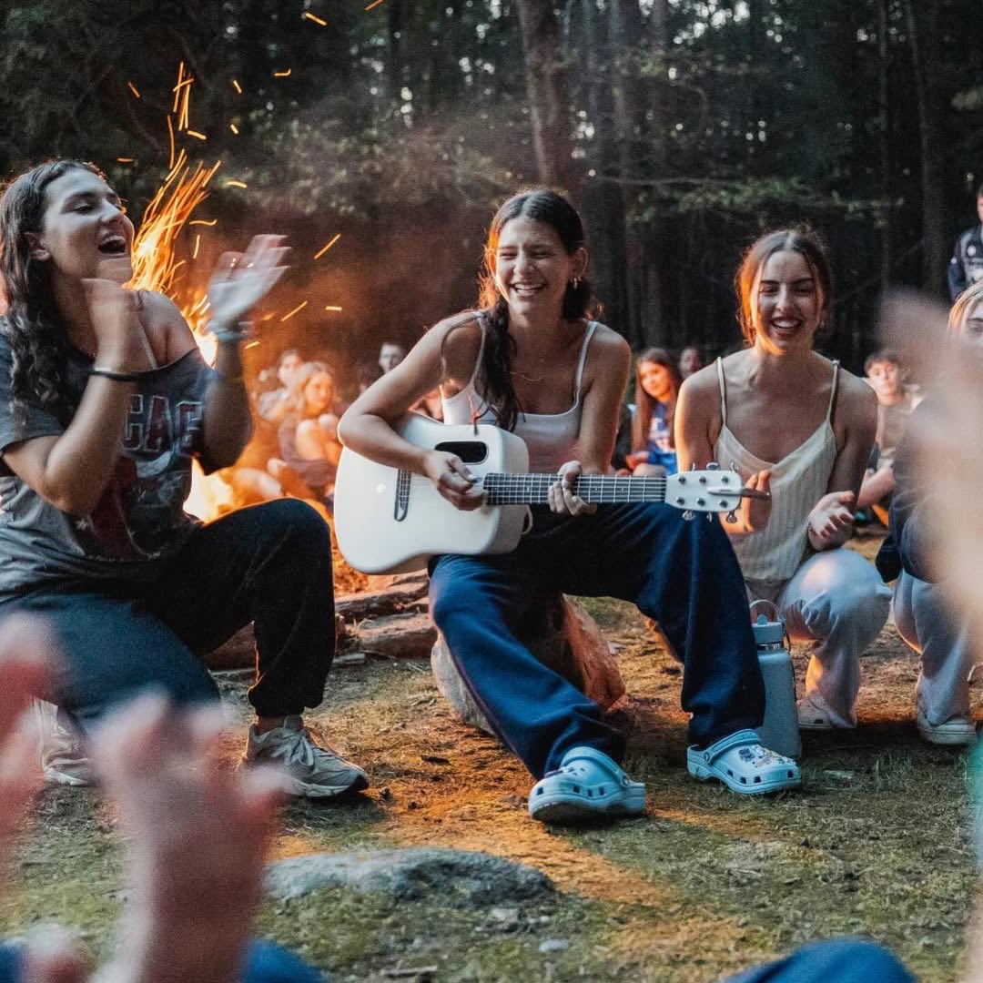 Teen campers singing around the campfire while one plays guitar