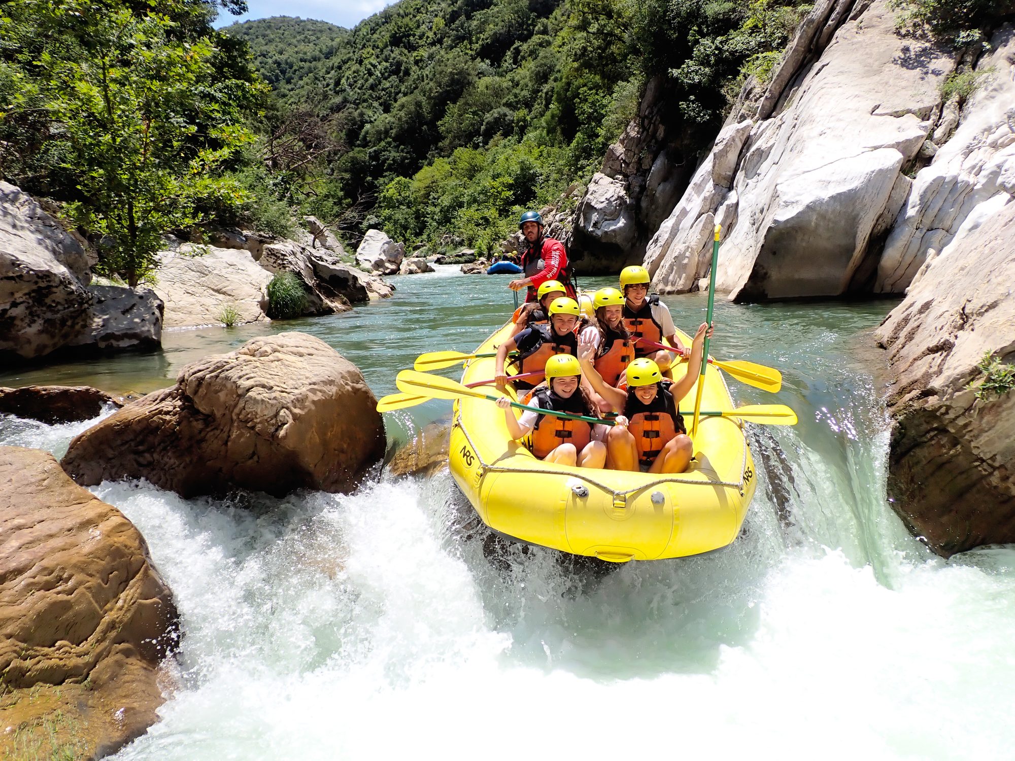 Teens paddling a yellow raft through whitewater rapids