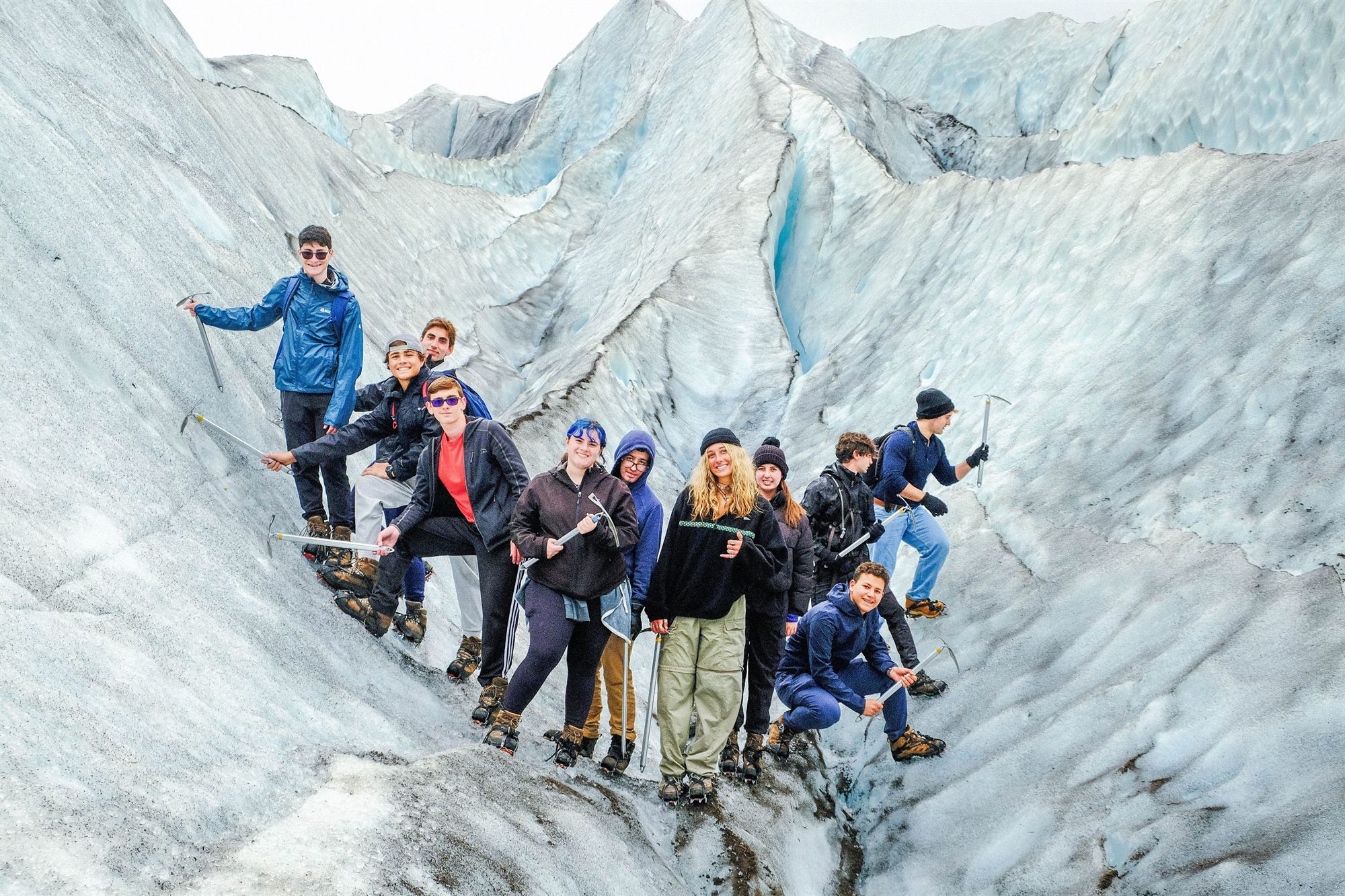 A group of teens in rain jackets hiking up through the ice on a glacier
