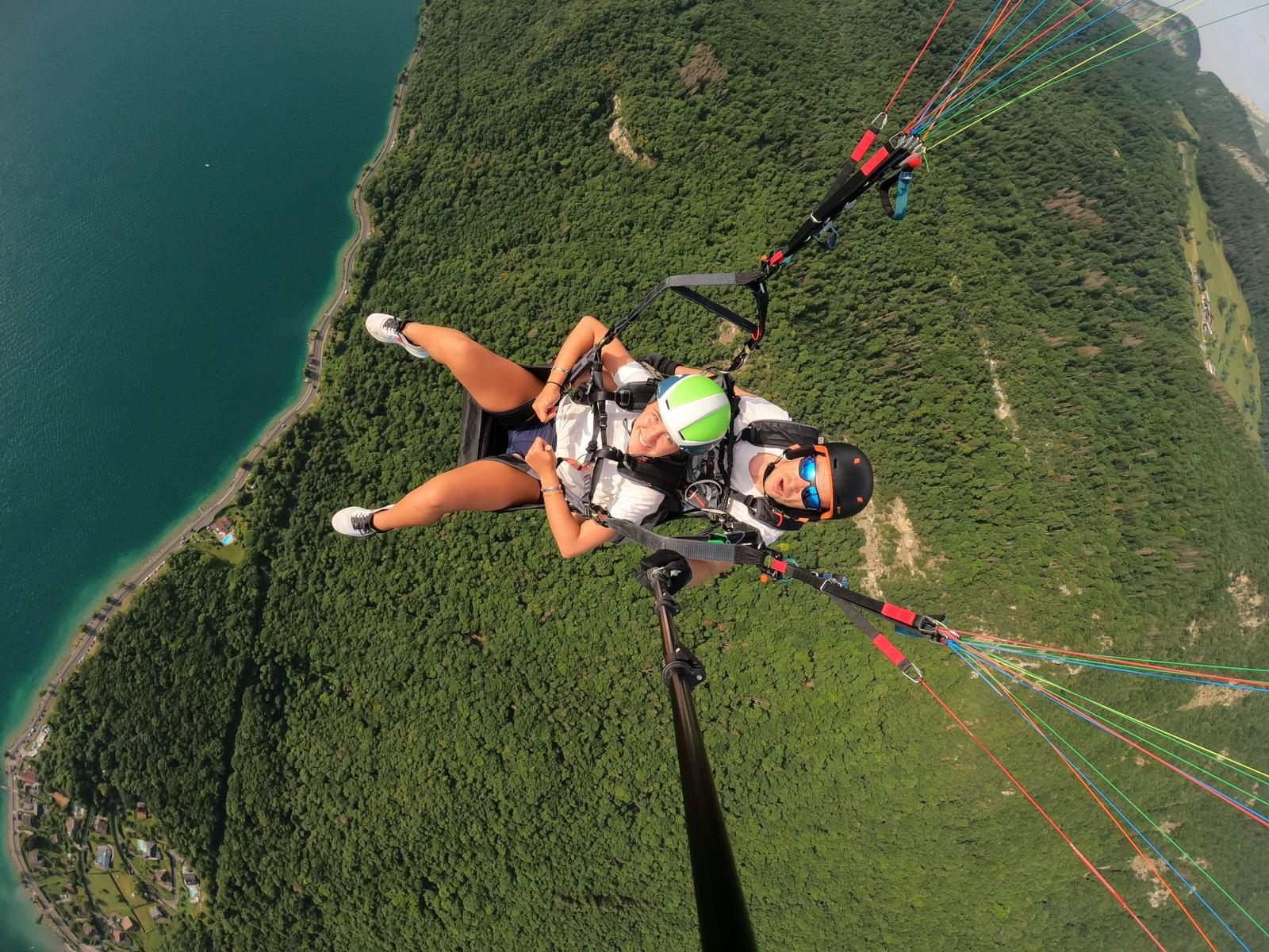 A teen tandem paragliding high above a lake and green mountainside