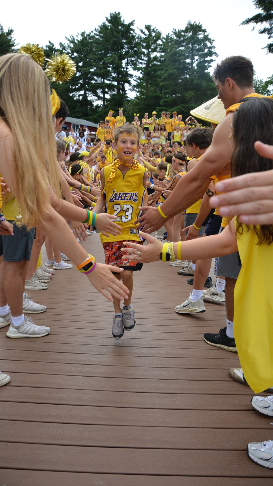 A young camper runs a high-five tunnel between rows of cheering campers dressed in yellow